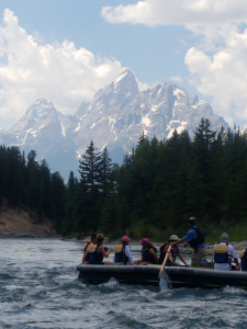 people in a boat on the river with trees and mountains