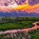A sunset over the Grand Teton mountains with a rustic fence and open field in the foreground.